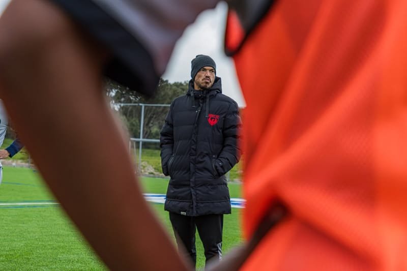 A Hope FC coach watching training from the touchline in club kit